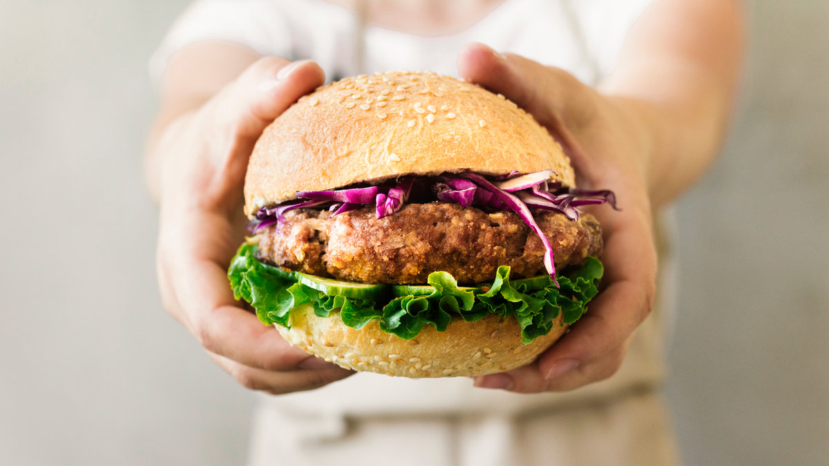 hamburguesa en primer plato sostenida por manos vegana plant based